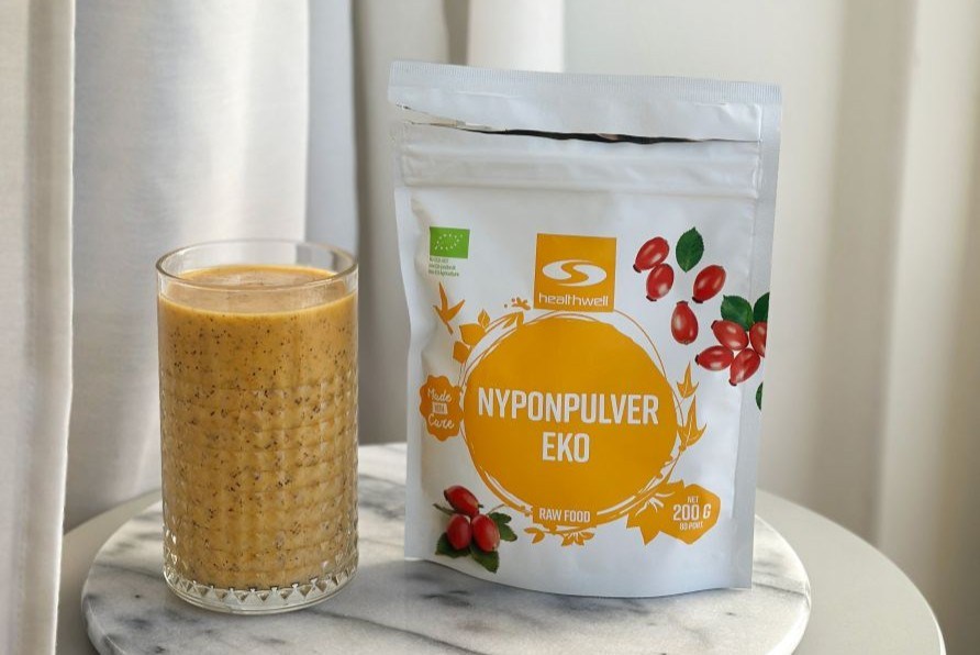 En frdig hyben, mango og passionsfrugt smoothie str ved siden af en Healthwell Hybenpulver KO pakke.